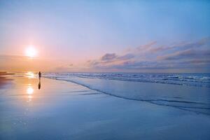 Fotografie de artă Person walking on beach at sunrise, Shannon Fagan, (40 x 26.7 cm)