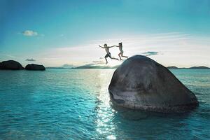 Fotografie de artă Two kids holding hands jumping off rock into sea, Gary John Norman, (40 x 26.7 cm)