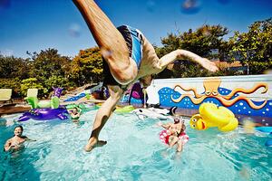 Fotografie Man in mid air jumping into pool during party, Thomas Barwick, (40 x 26.7 cm)