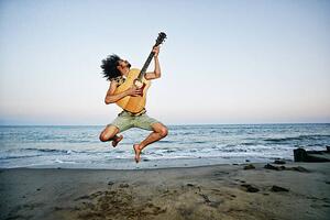 Fotografie Mixed Race man playing guitar and jumping at beach, Peathegee Inc, (40 x 26.7 cm)